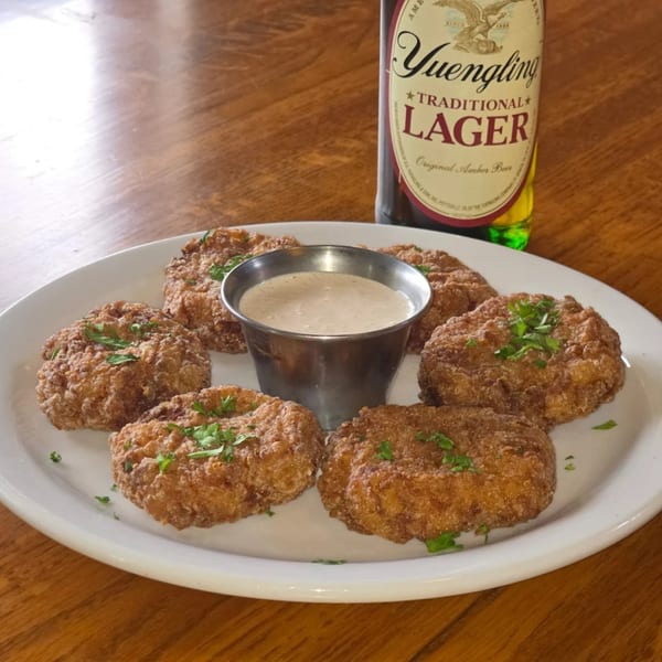 Fried appetizers with a dipping sauce and a bottle of Yuengling Lager on a wooden table.