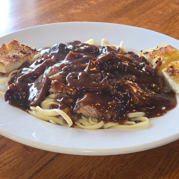 The Grill's American dish features noodles topped with a rich brown gravy, meat, and two pieces of garlic bread.