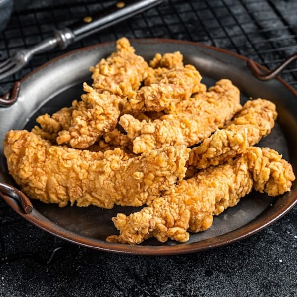 Crispy, golden-brown chicken tenders piled high on a dark metal serving tray.